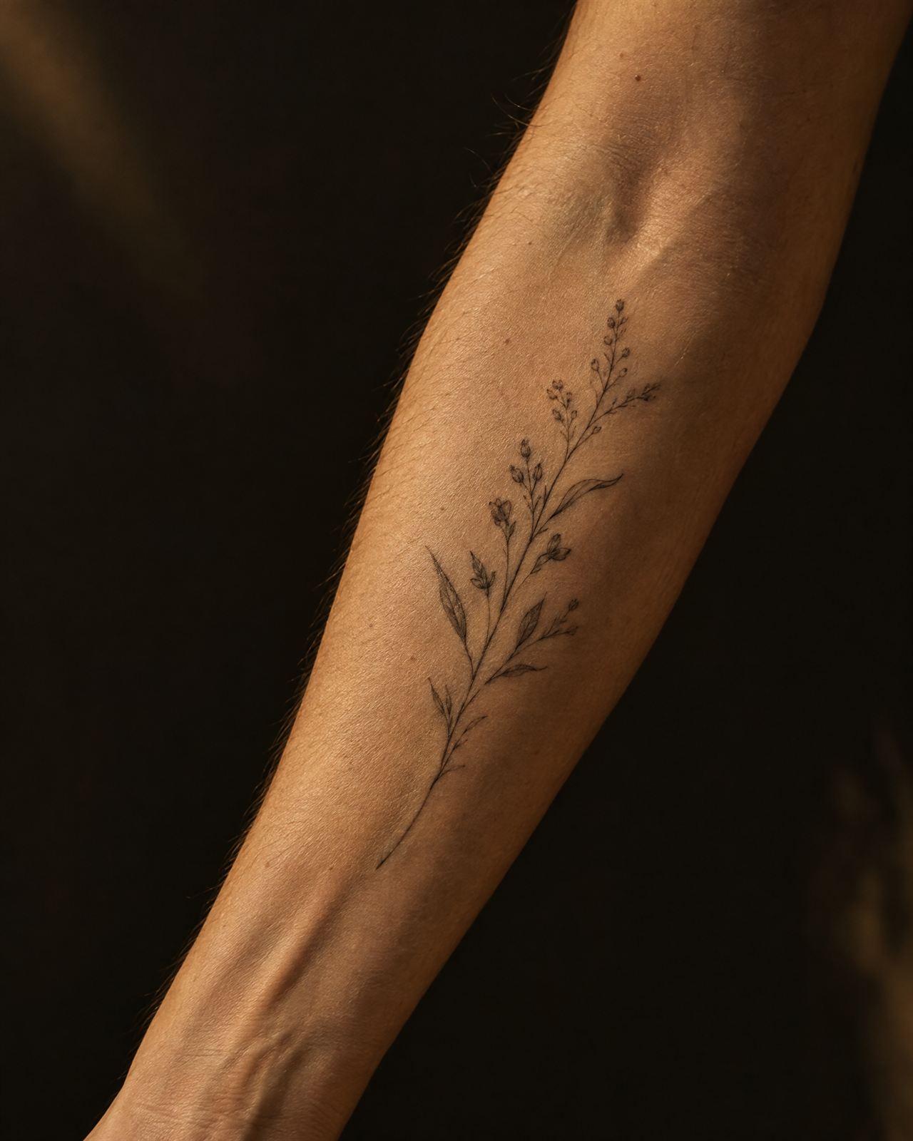Fine-line botanical tattoo on a forearm in warm light